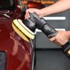 Cordless black dual action polisher with yellow foam pad being held up to polish a car.