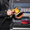 Dual action corded polisher in orange and black being grasped by a hand.